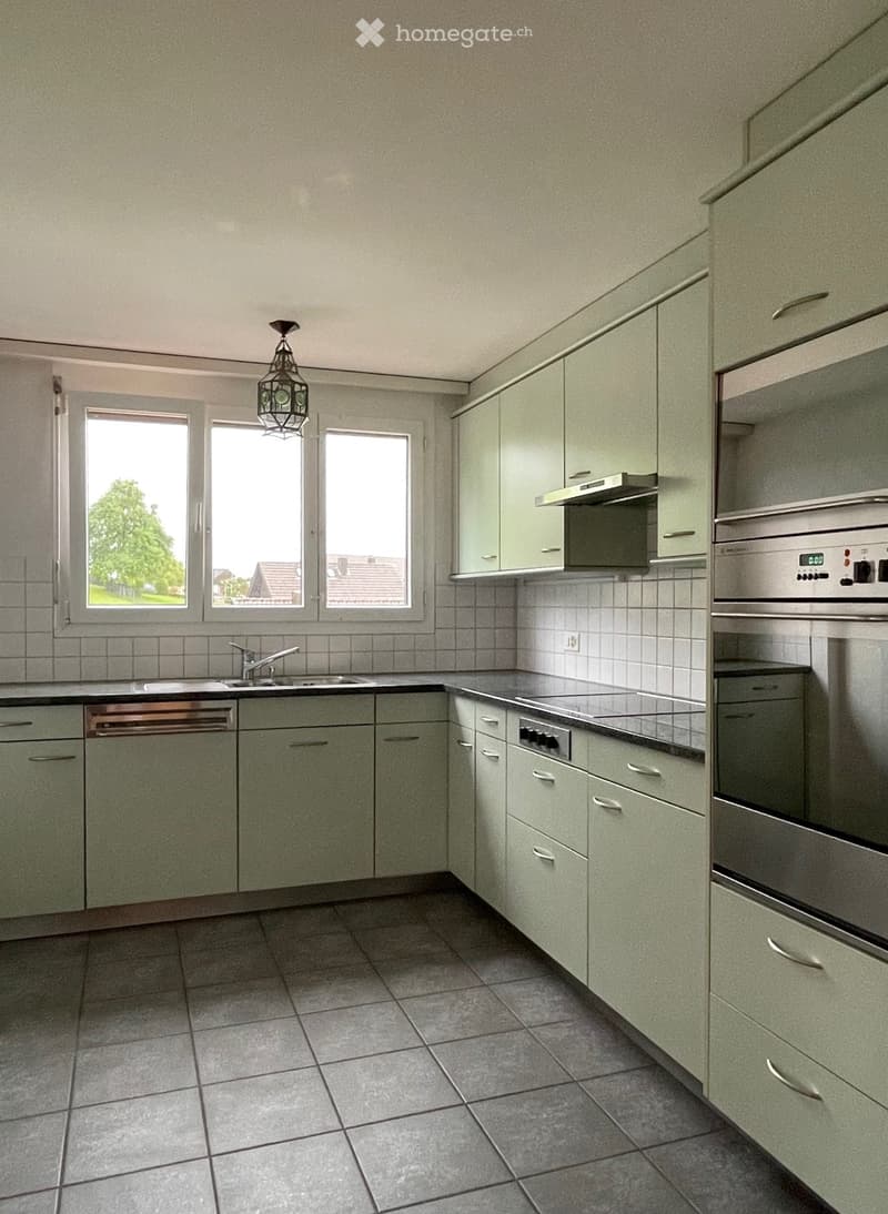Spacious kitchen with green cabinets, tile flooring, large windows, and a dishwasher