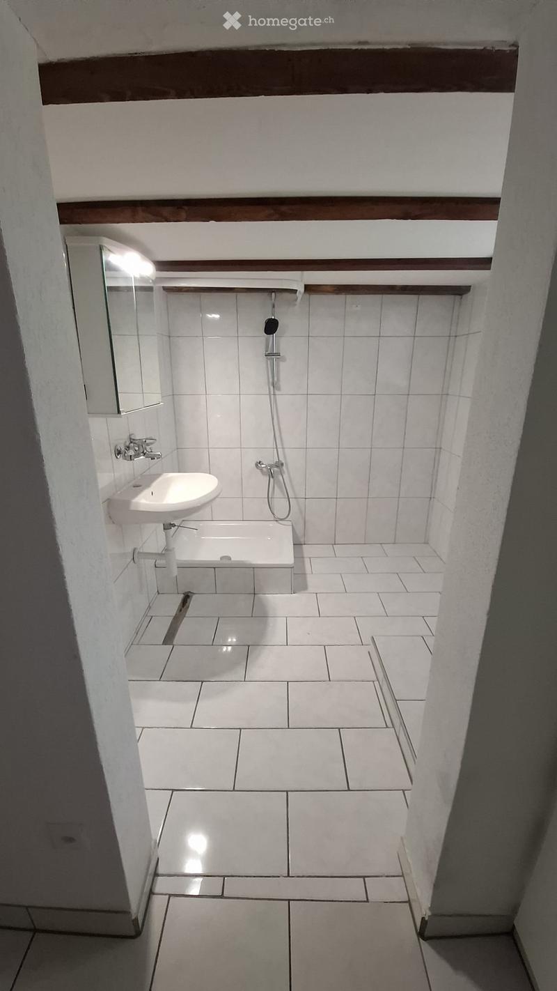 Small bathroom with tiled floor, white sink, shower, white walls, mirror above sink
