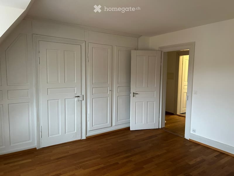 Empty room with wooden flooring, white walls, and multiple white doors.