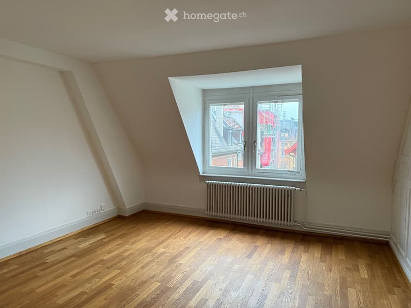 Empty attic room with wooden flooring, white walls, and a large skylight window offering a view of the city.