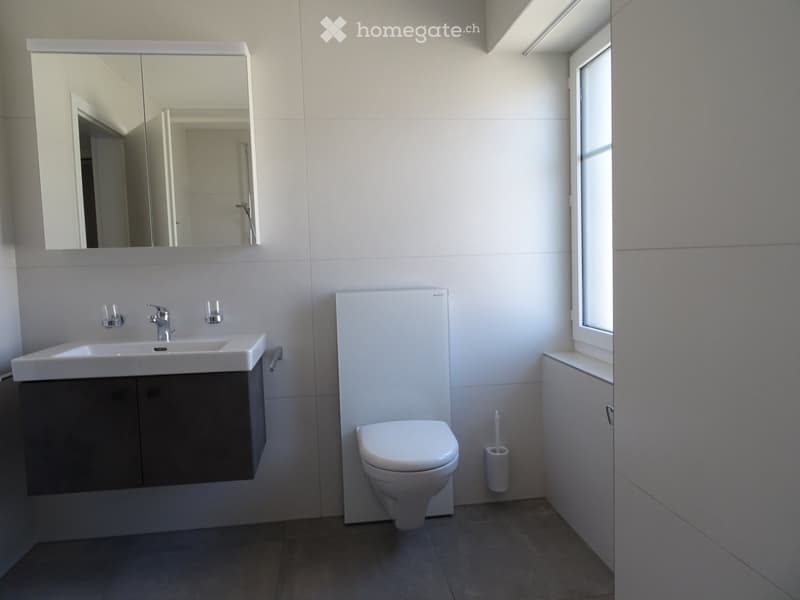Modern bathroom with a white sink, faucet, large mirror, toilet, and a small window letting in natural light.