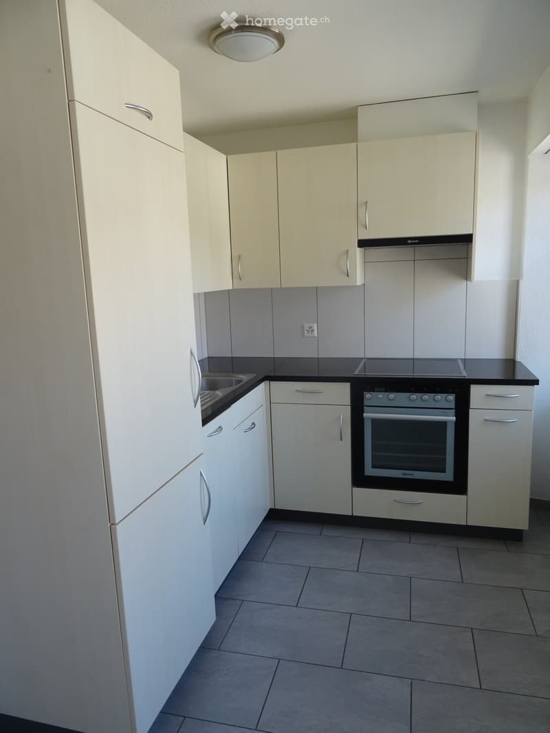Modern kitchen with white cabinets, stainless steel oven, sink, and tiled floor.