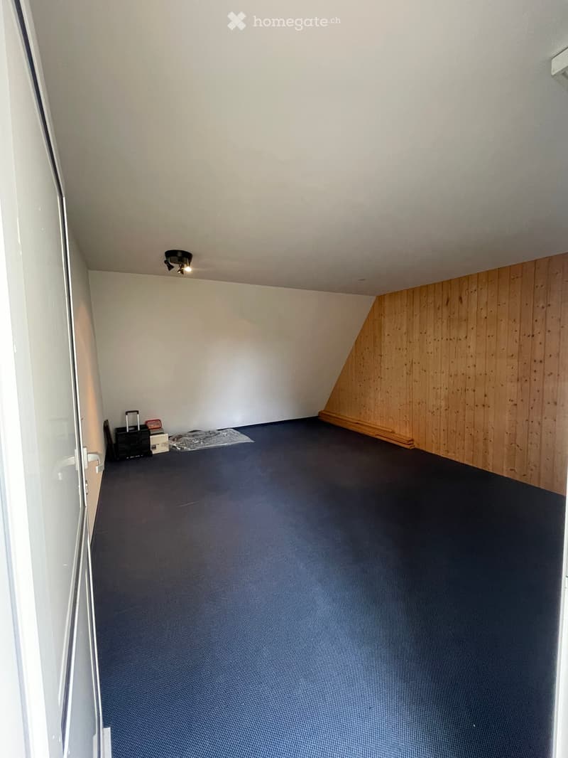 Empty room with blue carpet, white walls, wooden paneling on one side, and a small storage area with boxes and a suitcase.
