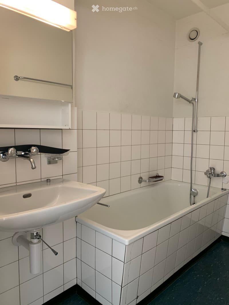 Modern bathroom with white tiled walls and floor, featuring a bathtub, sink, and showerhead.