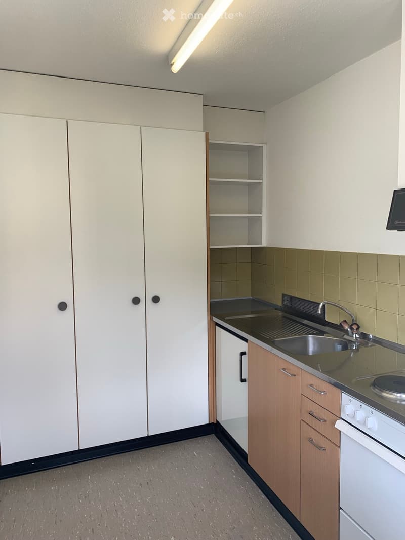 Modern kitchen with white and wooden cabinets, a sink with a faucet, a stove, and a small shelf unit.