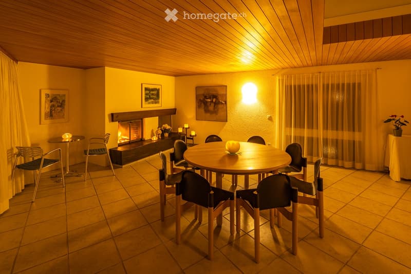 Dining area with a round wooden table, chairs, fireplace, and a small table with a candle