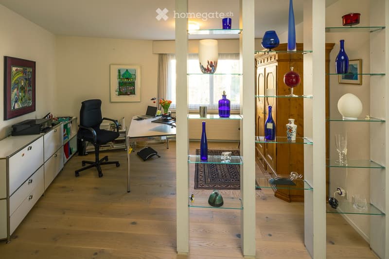 Office room with desk, chair, cabinet, shelves, paintings, and various decorative items.