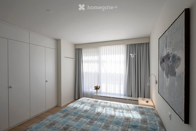 Bedroom with bed, white wardrobes, white walls, white floor, window with curtains, nightstand, lamp, painting