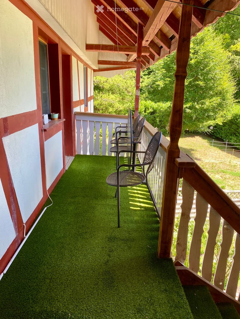 Balcony with artificial grass flooring, wooden railing, and a single black metal chair.