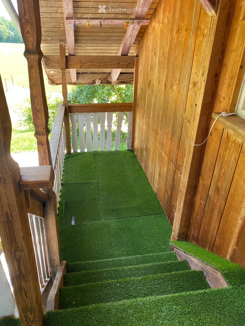 Wooden balcony with green artificial turf flooring, white balustrade, and wooden railings.
