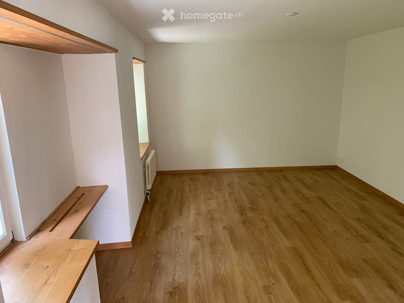 Empty room with wooden flooring, white walls, and built-in wooden shelves along one wall.