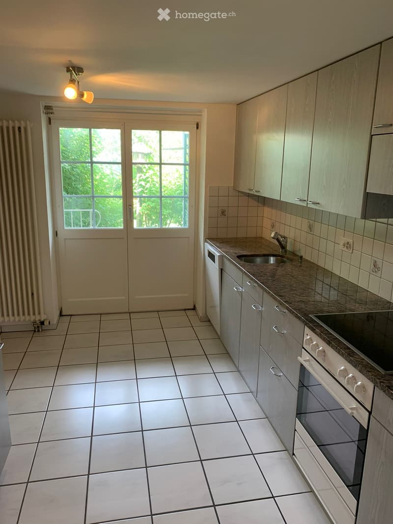 Modern kitchen with white tiled floor, light wood cabinets, granite countertop, sink, and built-in oven.