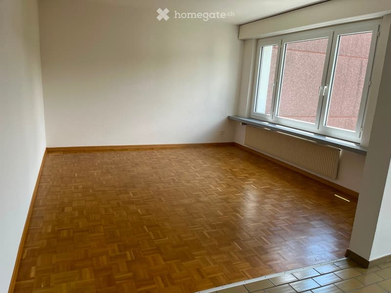 Empty room with wooden herringbone flooring, white walls, and large windows with frosted glass panels. A radiator is visible beneath the windows.