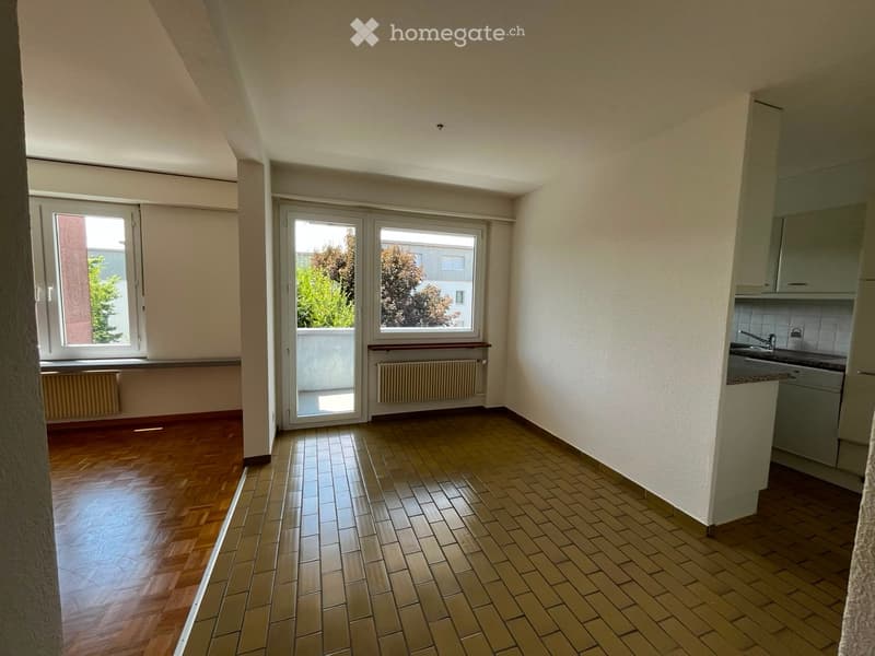 Bright, open room with wooden flooring, large windows, and a small kitchen area with a sink and cabinets.
