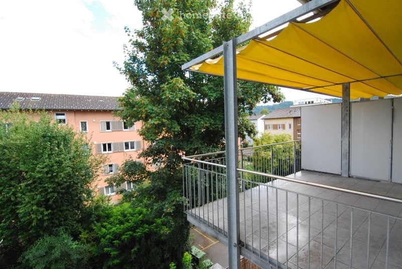 Balcony with metal railings and a retractable awning, surrounded by greenery.