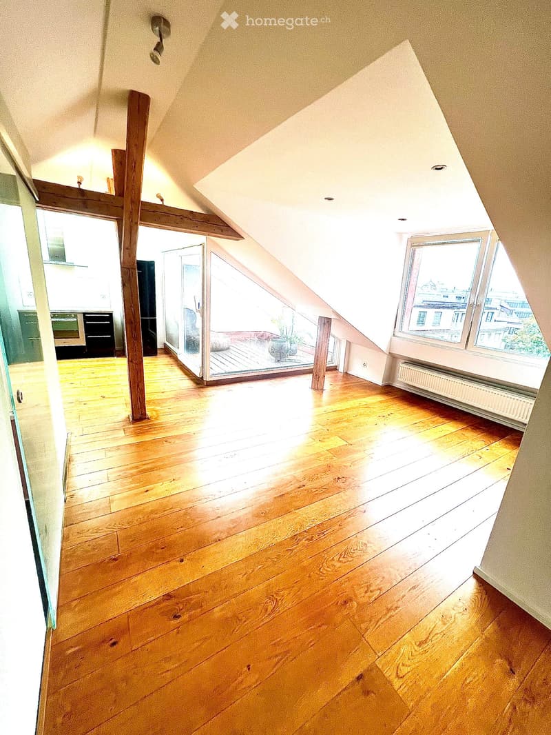 Open-plan living space with wooden floors, glass windows, and a view of the outside. There is a wooden cross structure in the middle of the room.