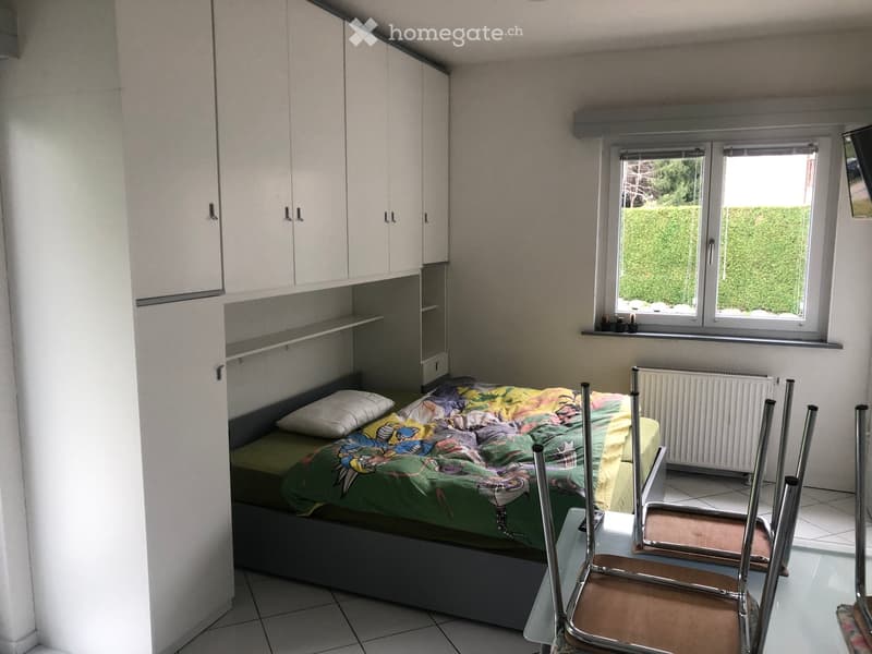 single bed, white storage units, radiator, windows with green garden view