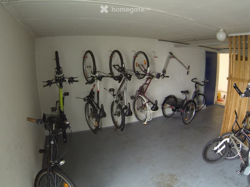 Garage with multiple bicycles hanging on wall racks and placed on the floor.