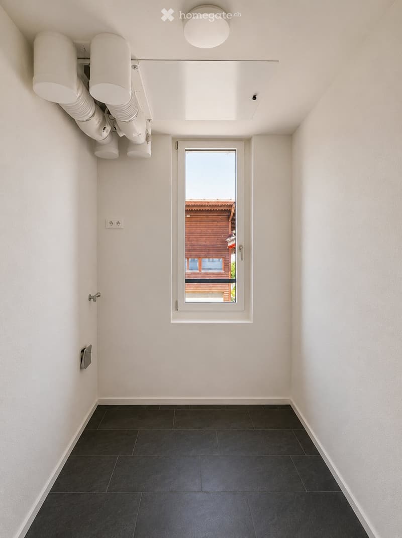 Empty hallway with white walls, dark tiled floor, and a large window showing a view of a wooden house and balcony outside.