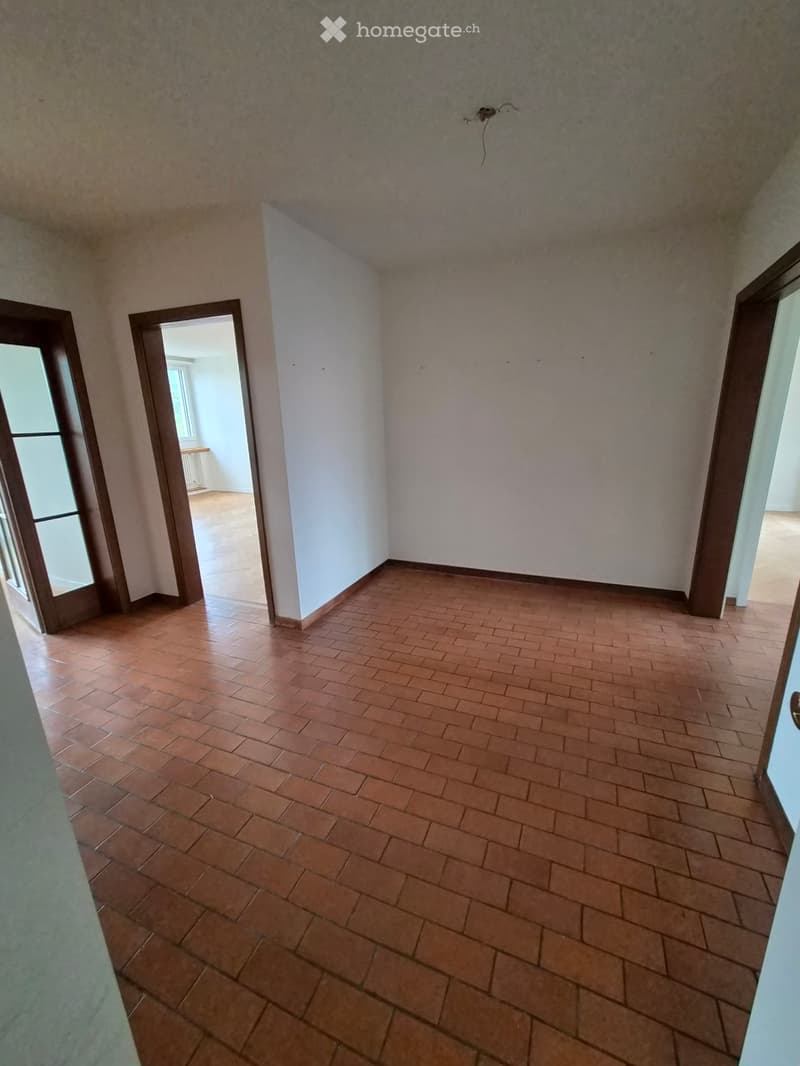 Empty room with tiled floor and white walls, featuring an open doorway leading to another room.