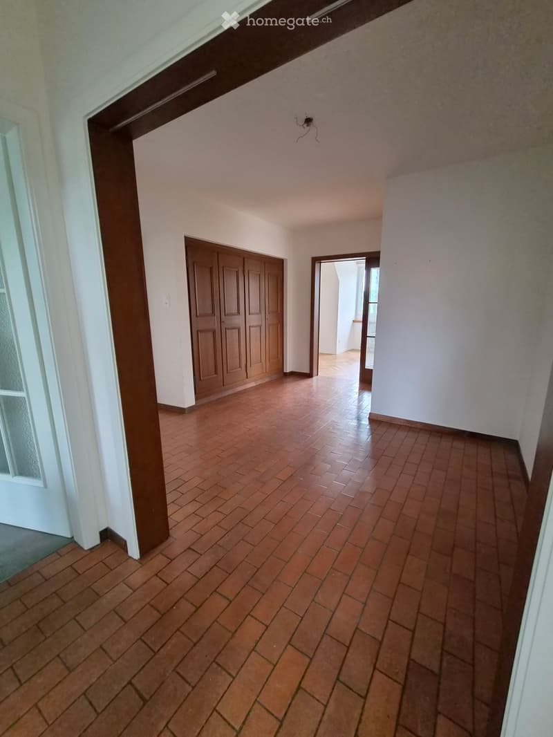 Empty hallway with tiled floor, white walls, and wooden doors leading to other rooms.