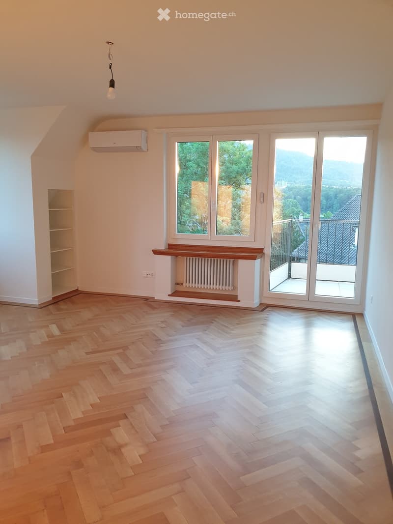 Empty room with wooden herringbone flooring, large windows, and a balcony with scenic views.