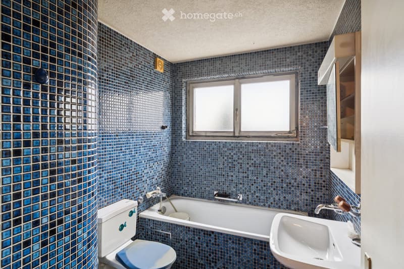 fully tiled bathroom, bathtub, toilet, sink, large window, storage cabinet
