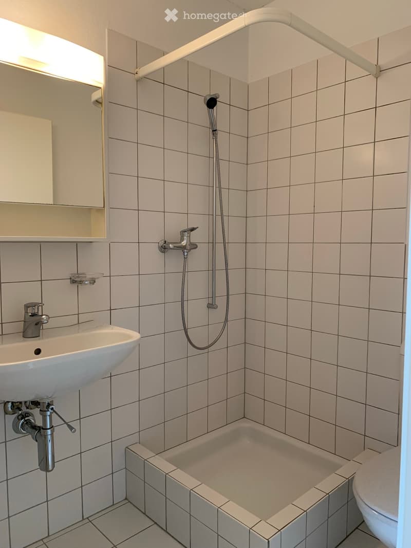 Modern bathroom with white tiled walls and floor, featuring a sink, bathtub, toilet, and showerhead.