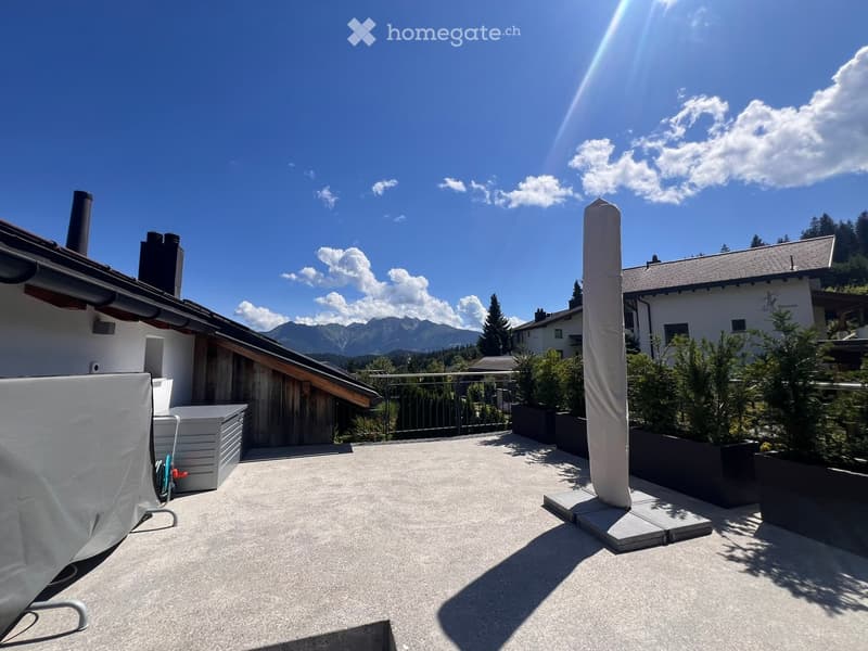 A spacious outdoor patio with a concrete floor, covered furniture, potted plants, and a scenic mountain view in the background.