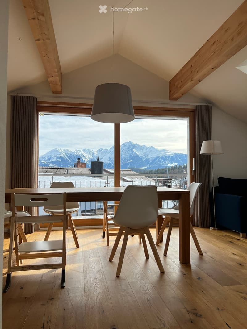 Bright dining area with wooden floor, large window offering mountain view, modern dining table and chairs, pendant lamp, and floor lamp.
