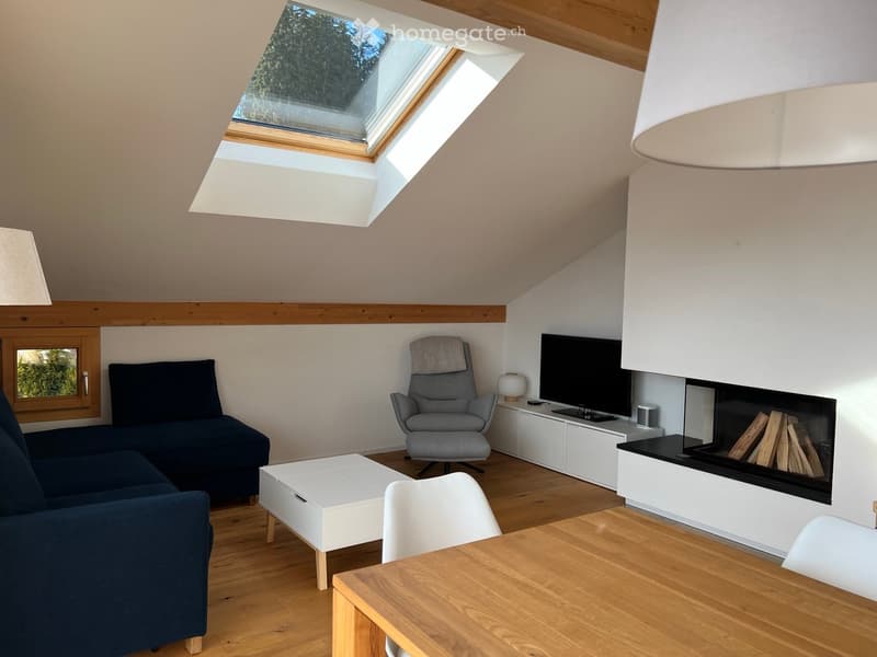 Modern living room with wooden flooring, a dark blue sofa, a white coffee table, a grey armchair, a fireplace, and a television on a white cabinet.