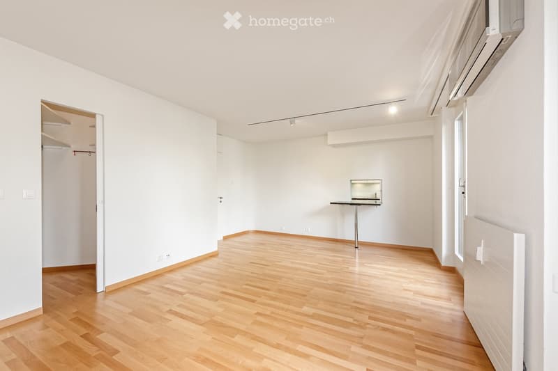Completely empty room with white walls, wooden floor, and a small built-in desk area with a mirror. No furniture or equipment.