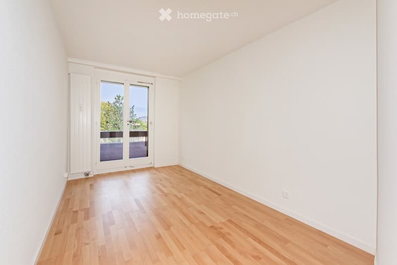 Empty room with light wooden flooring, white walls, and large sliding glass doors leading to a balcony.