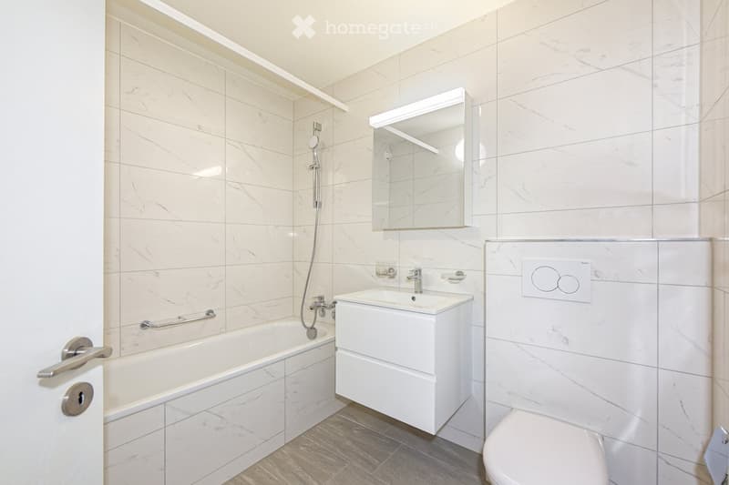 Modern bathroom with marble tiles, a bathtub, a sink with a modern faucet, a mirror cabinet, and a toilet.