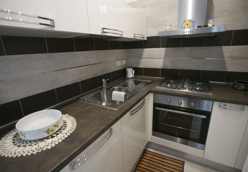 Modern kitchen with white cabinets, stainless steel appliances, dark countertops, and a decorative bowl on the counter.