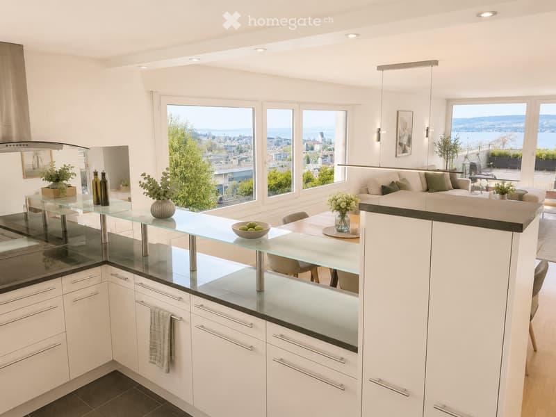 Modern open-plan kitchen and living area with white cabinets, glass countertop, integrated appliances, and large windows offering a scenic view.