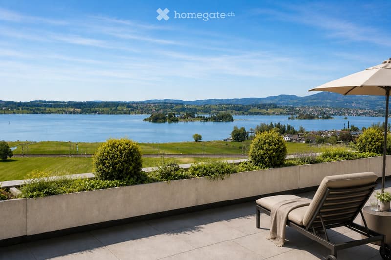 Balcony with a lounge chair, small table, umbrella, and scenic lake view.
