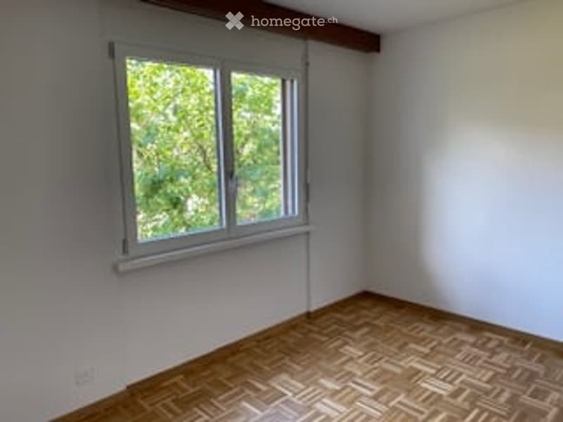 Empty room with wooden parquet flooring, white walls, and a single window with white frame and blinds.