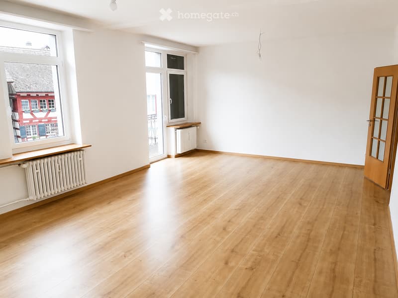 Empty room with wooden flooring, white walls, large windows, and radiators. No furniture or equipment present.