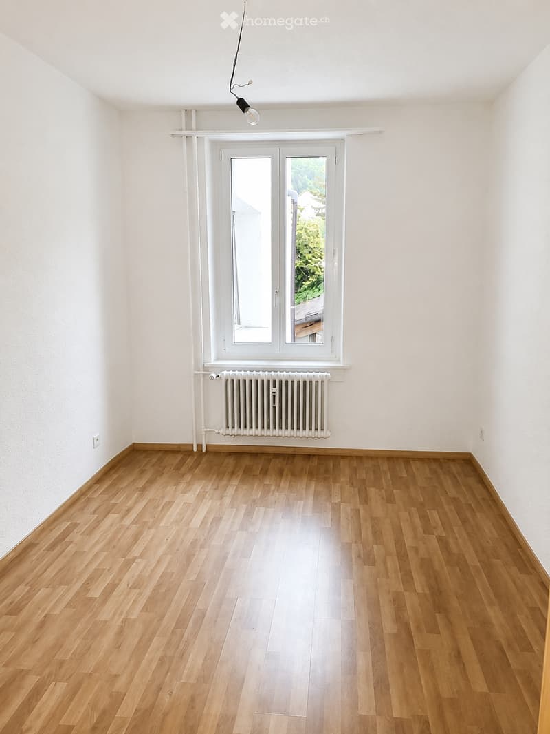 Empty room with wooden flooring, white walls, a window with double doors, a radiator, and a single light fixture on the ceiling.