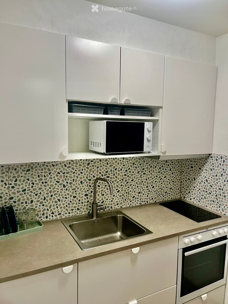 Modern kitchen with white cabinets, a mosaic tile backsplash, a stainless steel sink, and built-in appliances including a microwave and oven.