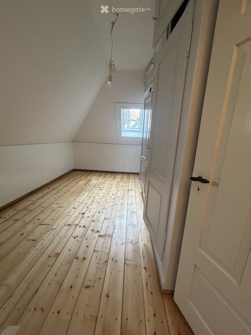 Empty hallway with wooden flooring, white walls, and a small window at the end.