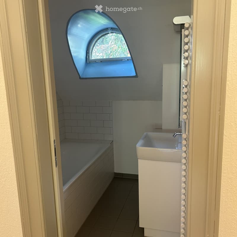 Modern bathroom with a bathtub, sink, and a large arched window offering a view of greenery outside.
