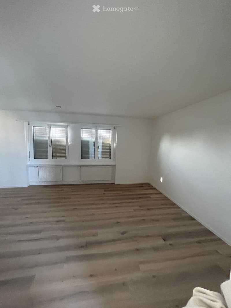 Empty room with wooden flooring, white walls, and large windows with blinds. No furniture or equipment present.