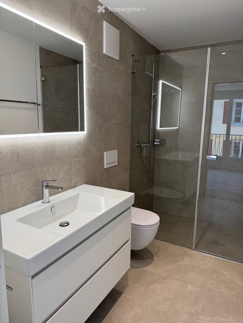 Modern bathroom with a white sink, chrome faucet, large mirror, toilet, and glass-enclosed shower area.