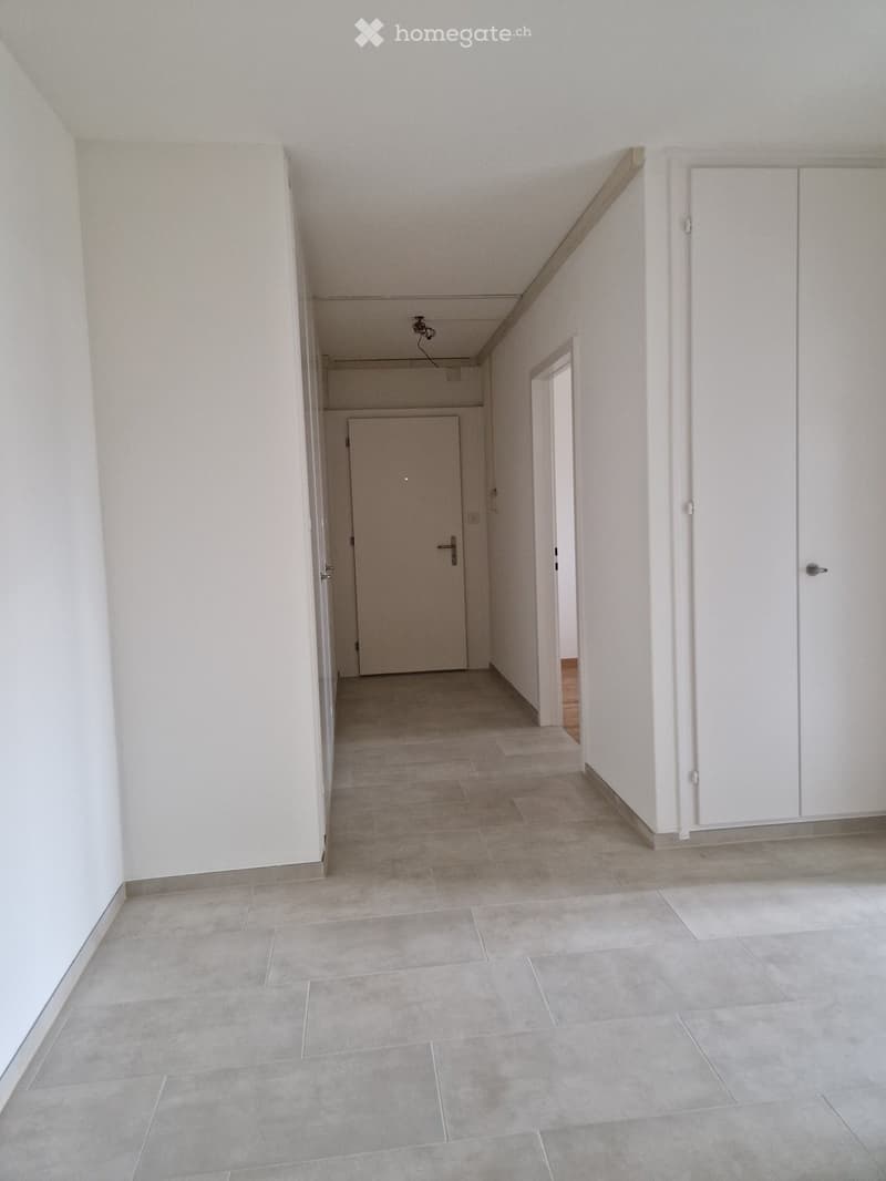 Empty hallway with white walls, tiled floor, and several doors leading to other rooms.