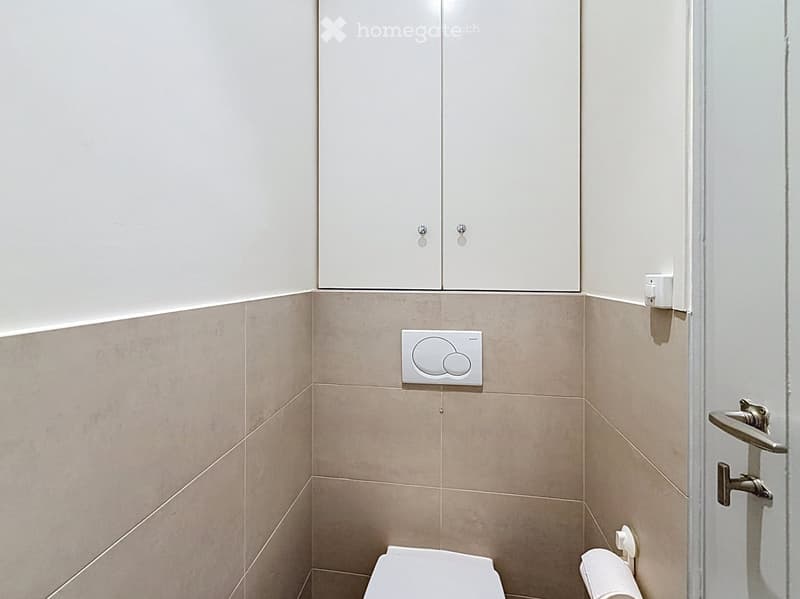 Modern bathroom with beige tiled walls, white cabinet above toilet, and a toilet seat.