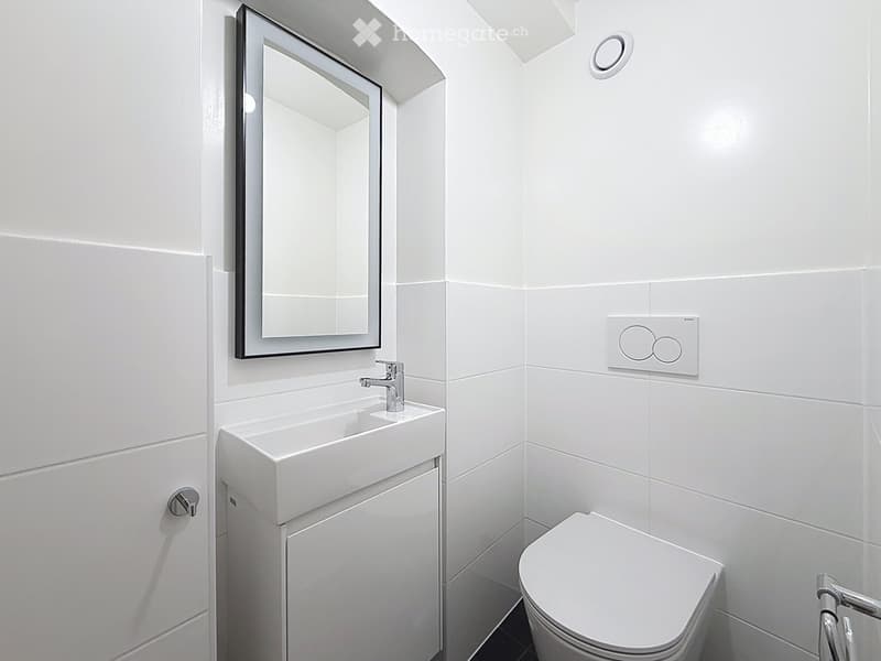 Modern white bathroom with a sink, mirror, and toilet. Features sleek fixtures and a minimalist design.