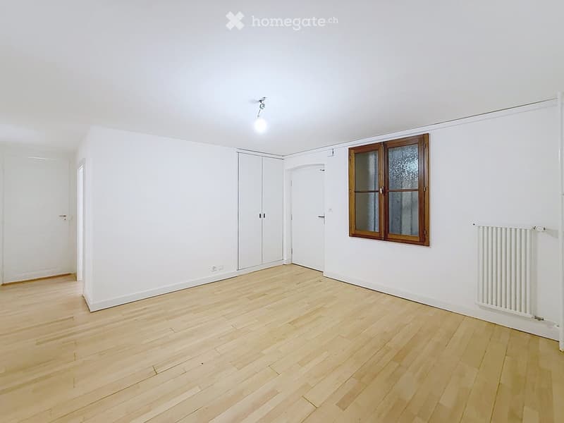 Empty room with light wooden flooring, white walls, a single window with frosted glass, and a radiator on one wall.