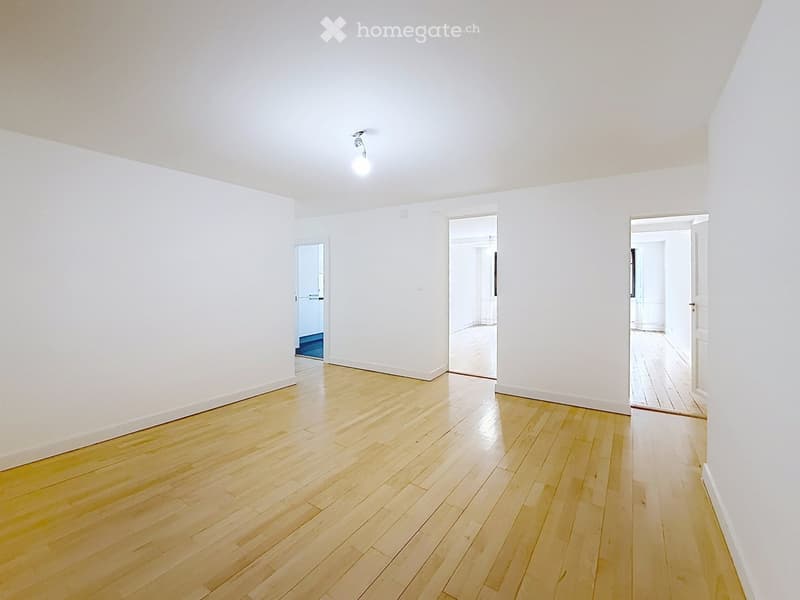 Empty room with white walls and wooden flooring, featuring three open doorways leading to other spaces.